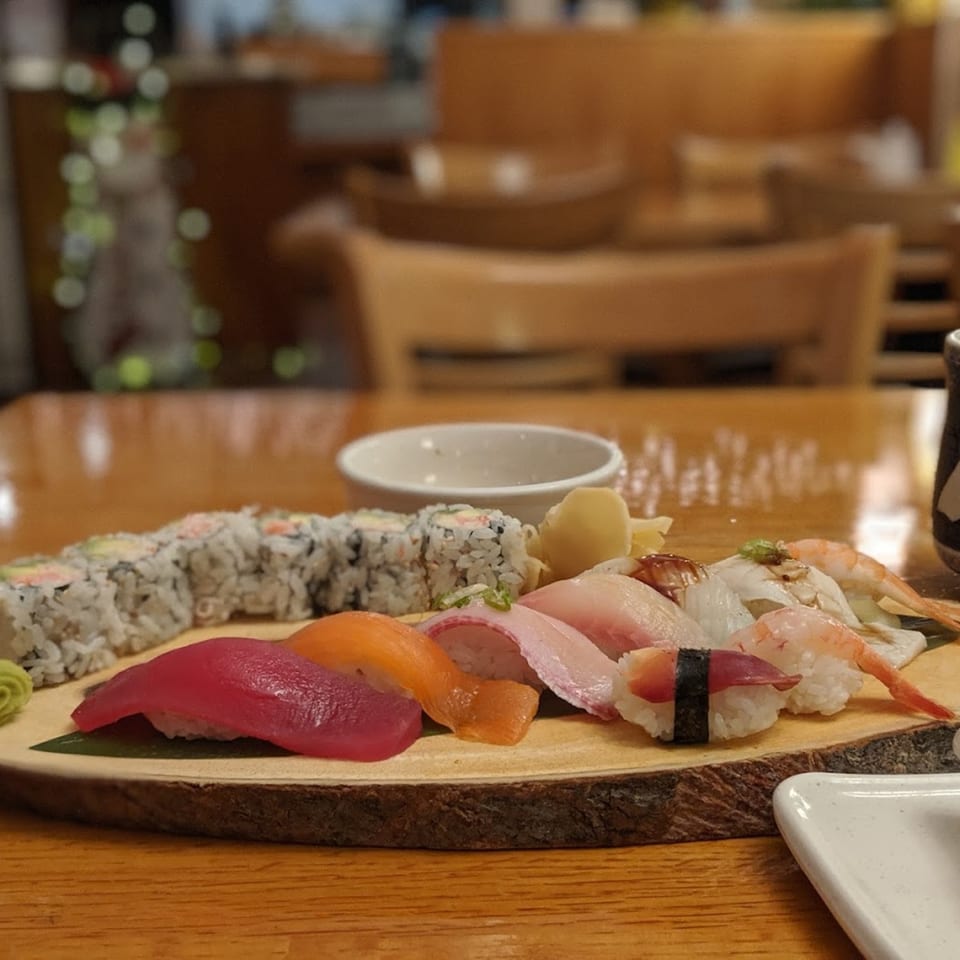 Assorted Tsunami Sushi rolls and nigiri on a wooden board, with a blurred restaurant background.