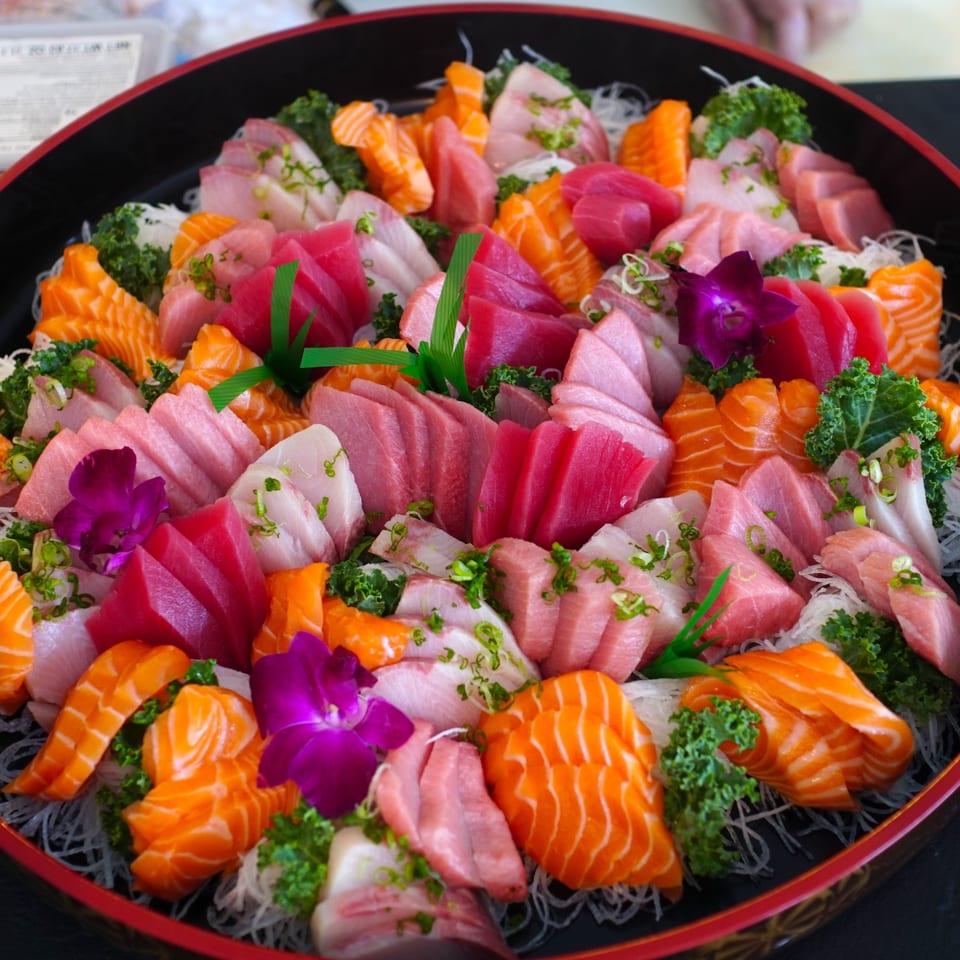 A large platter of Tsunami Sushi sashimi, featuring various cuts of tuna and salmon, garnished with orchids.