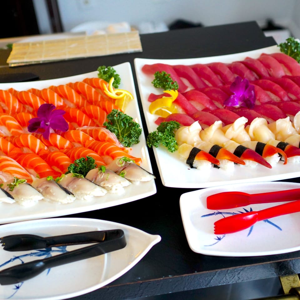 Platters of Tsunami Sushi's salmon, tuna, scallop, and clam nigiri, garnished with flowers and lemon.