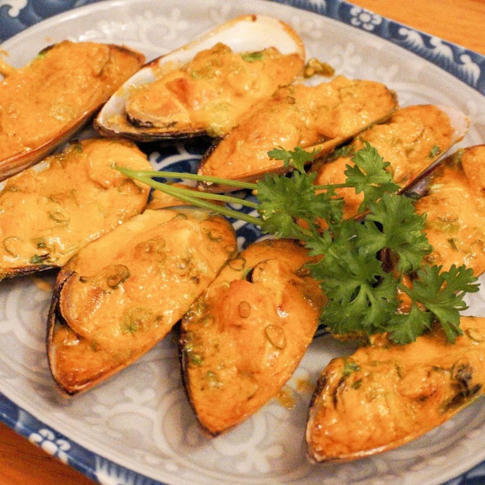 A platter of baked mussels topped with a creamy orange sauce and garnished with fresh parsley.