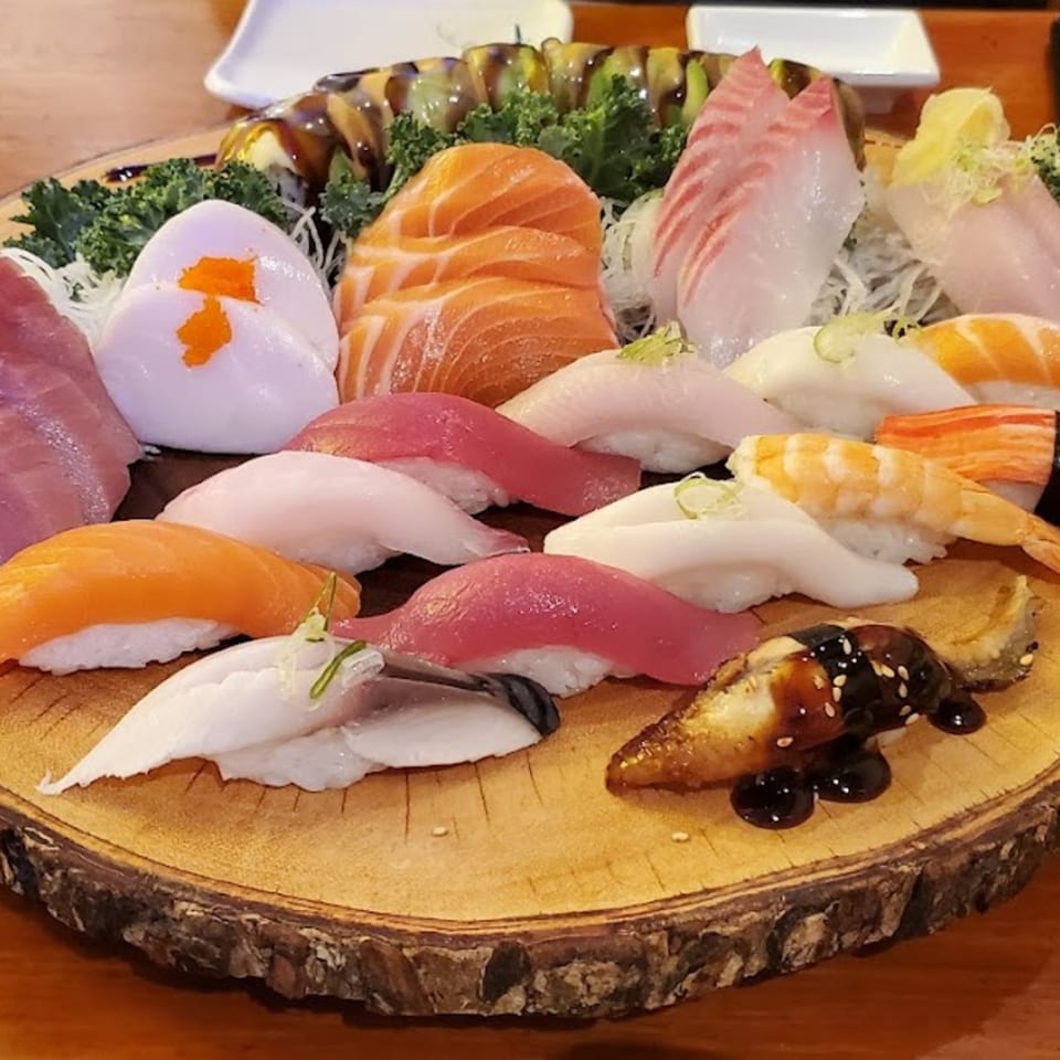 A large wooden platter overflowing with various Tsunami Sushi nigiri and sashimi, including salmon, tuna, and eel.