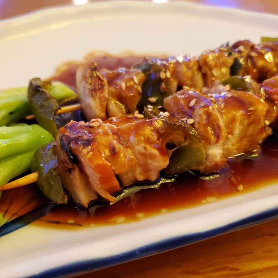 Two chicken and green pepper skewers with teriyaki sauce and sesame seeds on a white plate.
