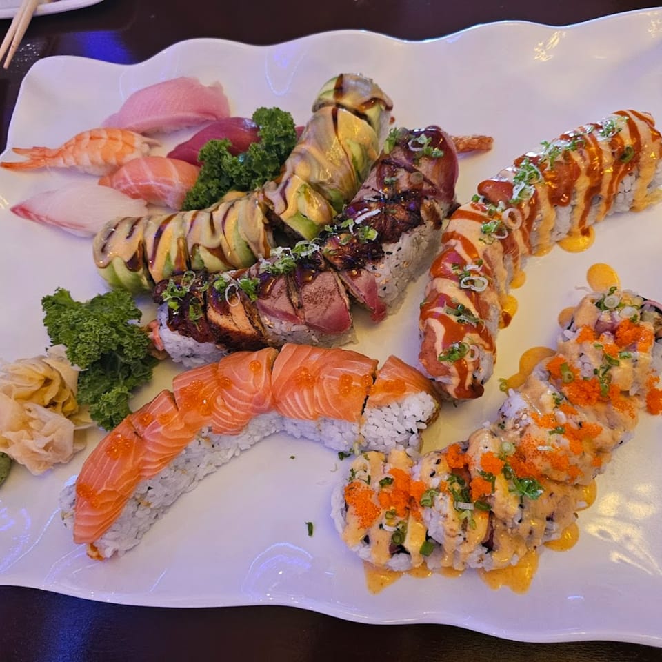 A large white platter filled with various Tsunami Sushi rolls, including nigiri, salmon, and avocado-topped rolls.